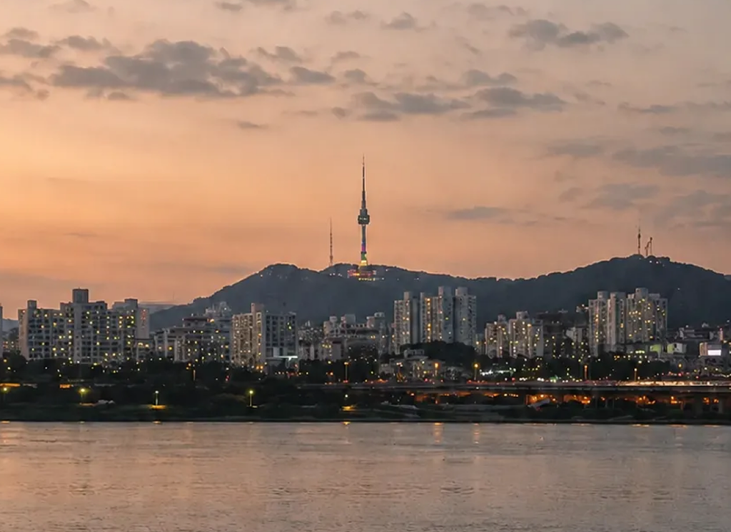 Han River picnic at sunset in Seoul with a peaceful riverside view, city skyline, and N Seoul Tower in the distance, showcasing one of the best Seoul picnic spots and a complete Han River park guide.