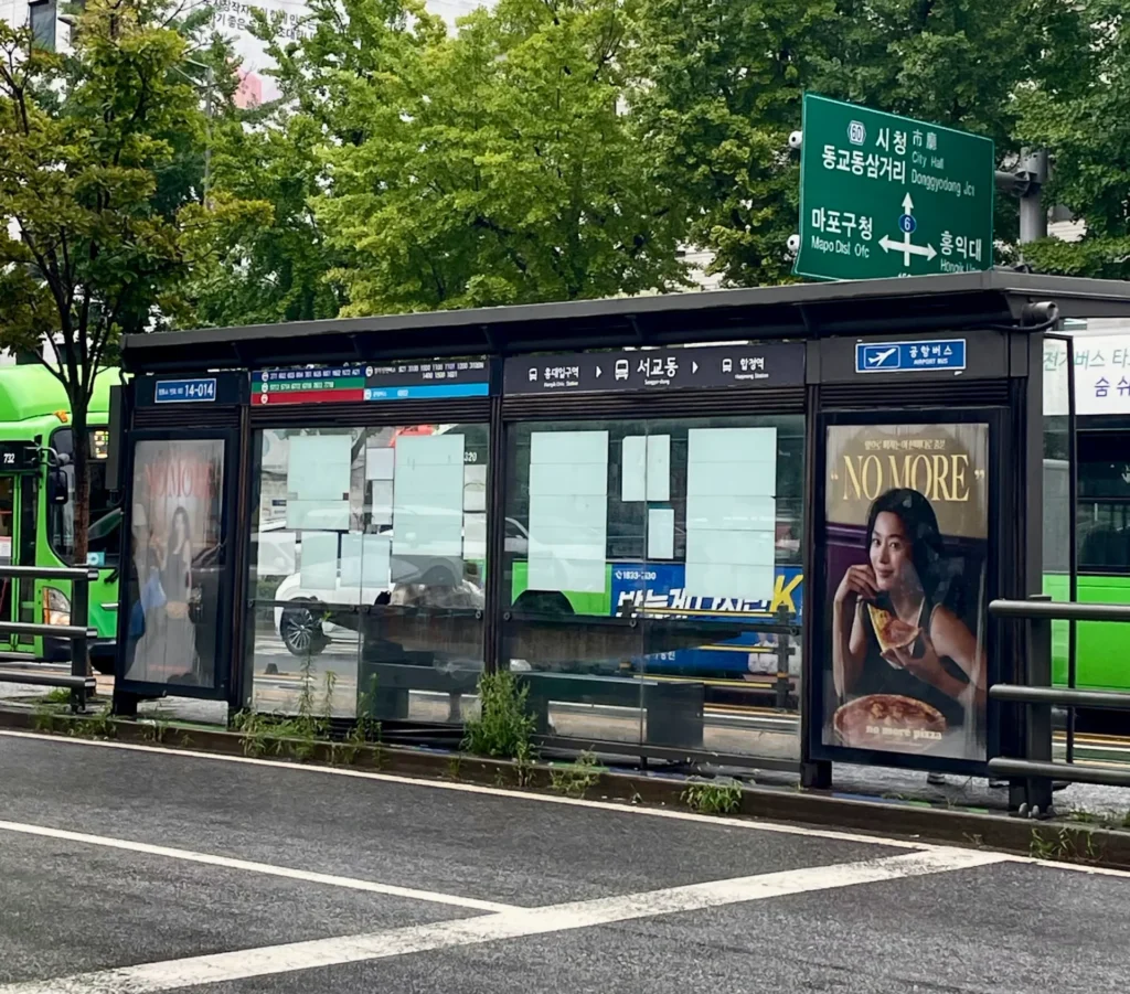 Seoul city bus stop with route maps and green buses, illustrating how to ride Seoul bus and find the correct bus stop in Korea.