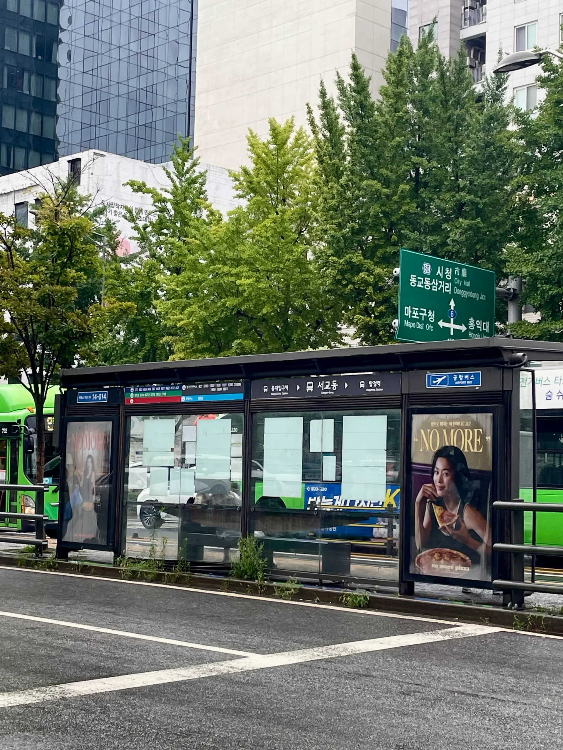 Korea rainy season at a modern Seoul bus stop with wet streets, green city buses, lush trees, and reflective pavement in a calm urban atmosphere